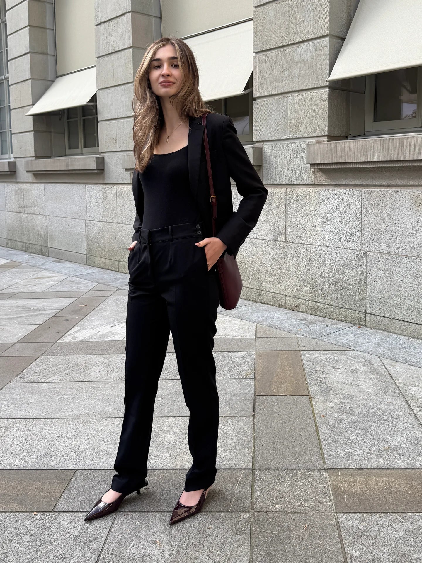 Black pants with a black blazer, burgundy shoulder bag and pointed heels.